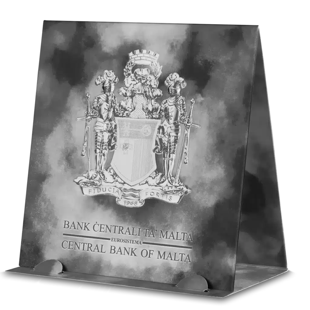 The 2023 Knights of the Past 5 Euro 1 oz Silver BU features the Malta coat of arms and “Bank Ċentrali ta’ Malta Eurosistema Central Bank of Malta” on a silver plaque, standing upright on a clear triangular base.