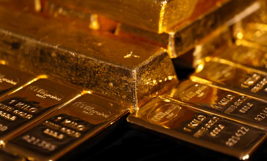 Varios lingotes de oro brillante están apilados, con algunos marcados con 1 KILO y otros números identificativos visibles. Los lingotes reflejan la luz, resaltando su intenso color dorado.