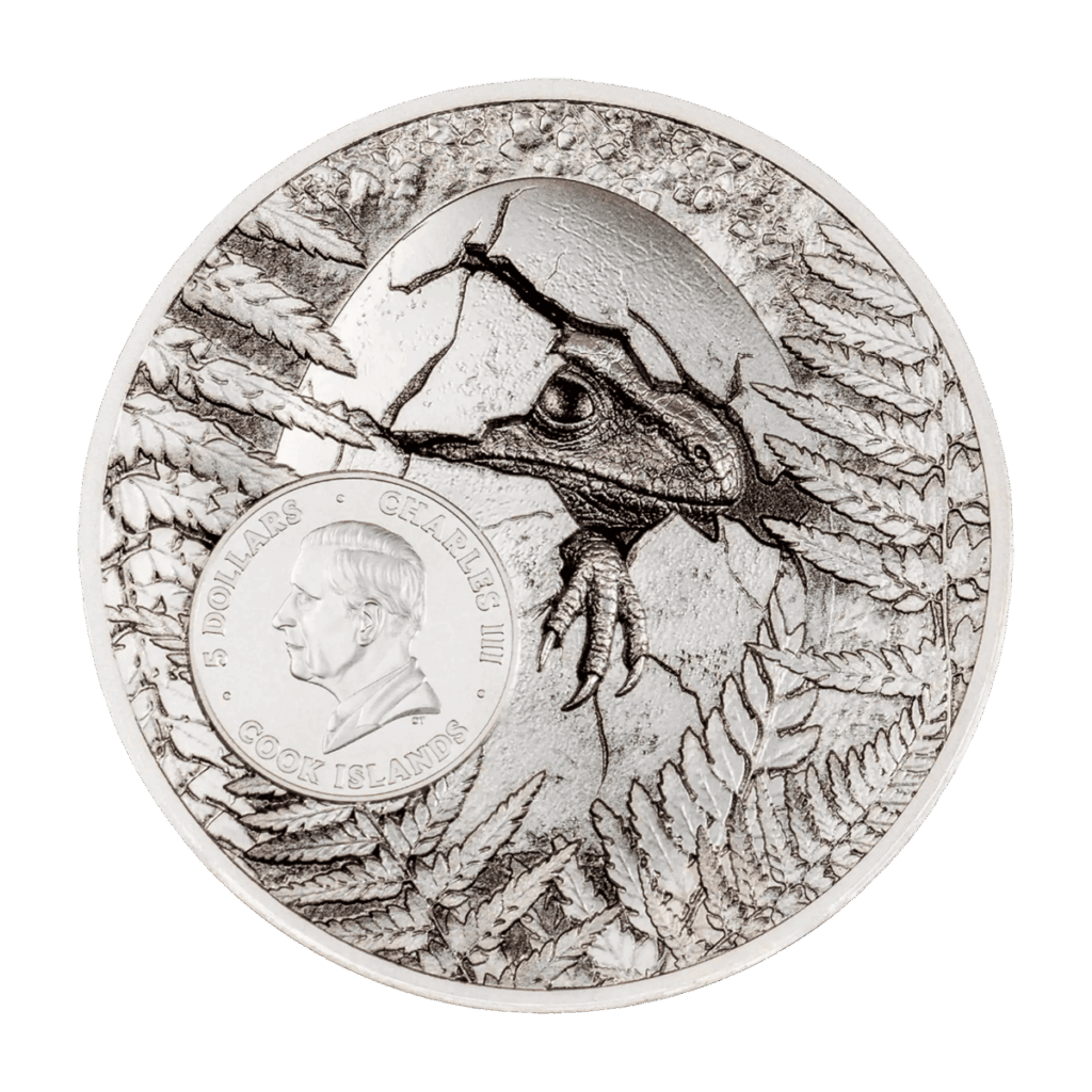 Retro della moneta da collezione "Jurassic Relics – Carcharodontosaurus" Italpreziosi in argento delle Isole Cook da 5 dollari. Incisione di un dinosauro che fuoriesce da un uovo schiuso tra felci preistoriche, con medaglione centrale recante il ritratto di re Carlo III e iscrizione "Charles III · 5 Dollars · Cook Islands".