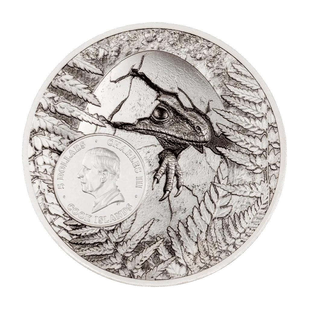 Back of the "Jurassic Relics – Carcharodontosaurus" Italpreziosi silver collectible coin, Cook Islands 5 dollars. Engraving of a dinosaur hatching from a cracked egg among prehistoric ferns, with a central medallion bearing the portrait of King Charles III and the inscription "Charles III · 5 Dollars · Cook Islands". 