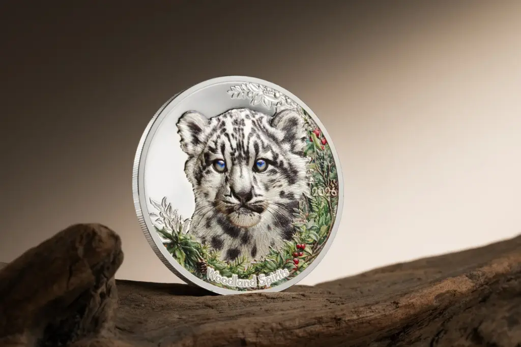 Moneta Woodland Spirits - Leopardo delle Nevi 1 oz argento in piedi su un tronco di legno, con il cucciolo colorato in primo piano e sfondo caldo sfumato.