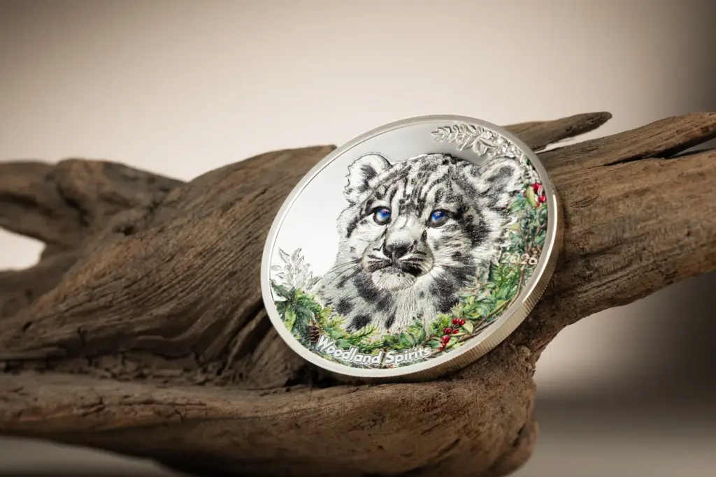 Moneta Woodland Spirits - Leopardo delle Nevi 1 oz argento appoggiata in diagonale su un tronco, che mostra la colorazione dettagliata del leopardo e del sottobosco.