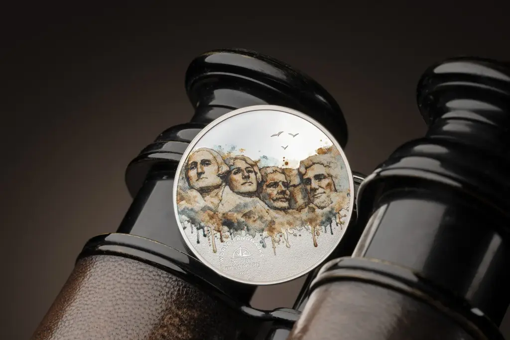 Moneta World Landmarks - Monte Rushmore 1/2 oz argento appoggiata su un binocolo vintage in ottone e pelle, con il design ad acquerello dei quattro presidenti in primo piano.