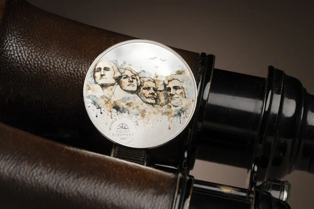 Moneta World Landmarks - Monte Rushmore 1/2 oz argento inclinata su un binocolo vintage, che mostra le colature di colore e lo sfondo dall'aspetto cartaceo.