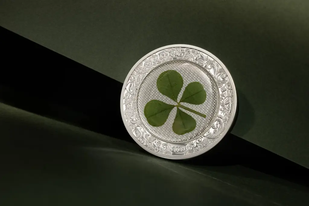 Moneta Ounce of Luck 2026 in argento con quadrifoglio vero integrato, in piedi su fondo verde scuro attraversato da una lama di luce.