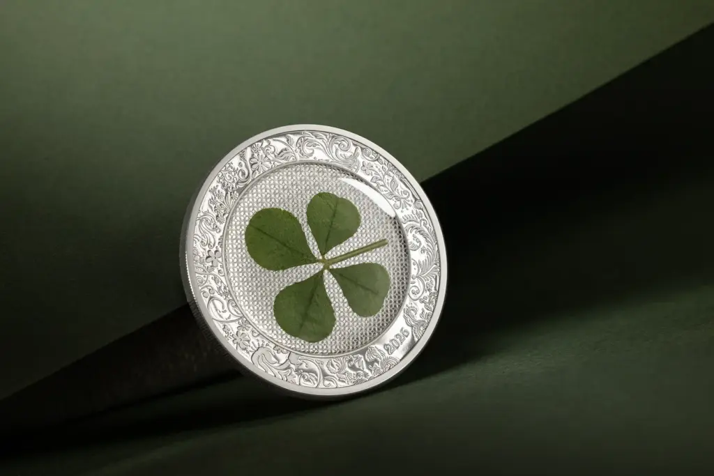 Moneta Ounce of Luck 2026 in argento ripresa di tre quarti su fondo verde, che mostra il quadrifoglio incastonato e il bordo decorato a rilievo.