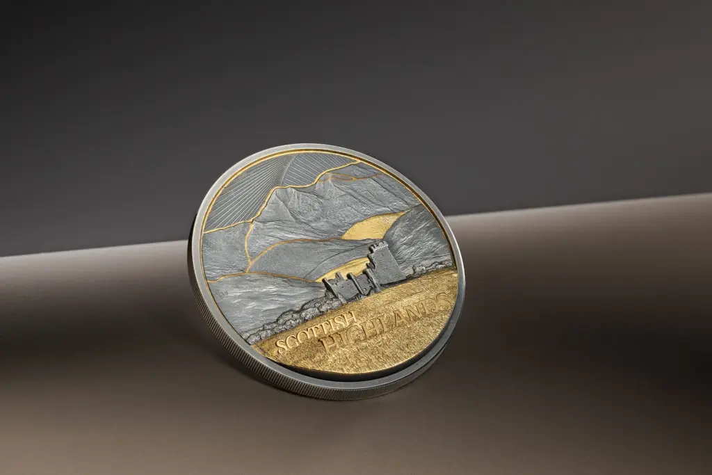 Moneta Golden Landscapes - Scottish Highlands 2 oz argento inclinata su fondo neutro, con il castello in rovina e le montagne in ultra alto rilievo illuminati di taglio.