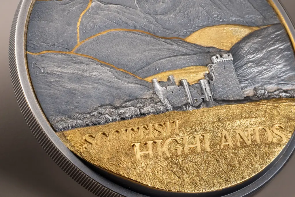 Macro della moneta Golden Landscapes - Scottish Highlands 2 oz argento: dettaglio del castello in rovina, del muretto a secco e della brughiera dorata con la scritta SCOTTISH HIGHLANDS in rilievo.
