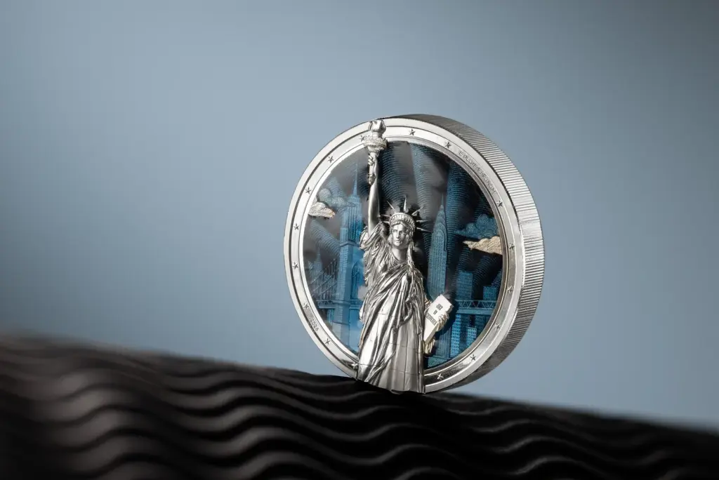 Moneta Timeless Icons - Statua della Liberta 2 oz argento in piedi su una superficie ondulata nera, con la statua in altorilievo che emerge dal fondo blu smaltato.