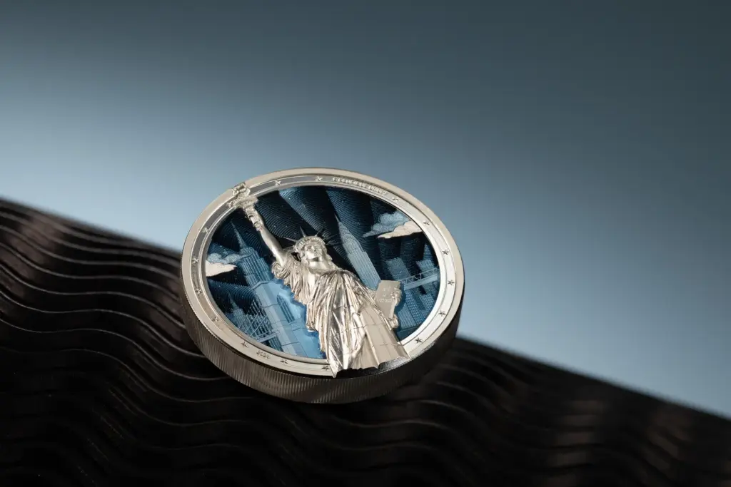 Moneta Timeless Icons - Statua della Liberta 2 oz argento ripresa di tre quarti, che mostra il rilievo della statua sporgere oltre il tondello e lo skyline azzurro sullo sfondo.